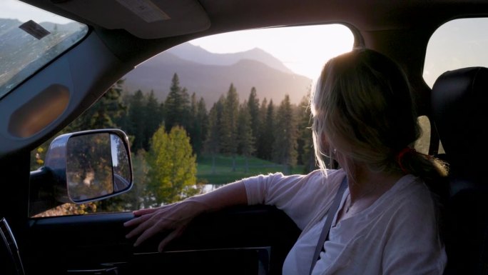成熟女子在副驾驶座位上放松，用智能手机拍下山景