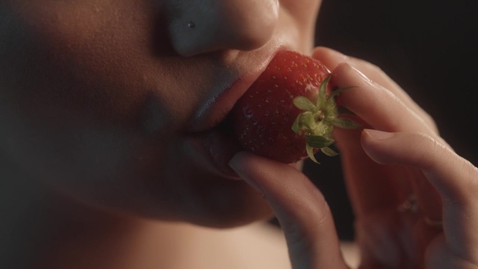 性感的女人用红色的口红工作室拍摄咬一口草莓和品尝