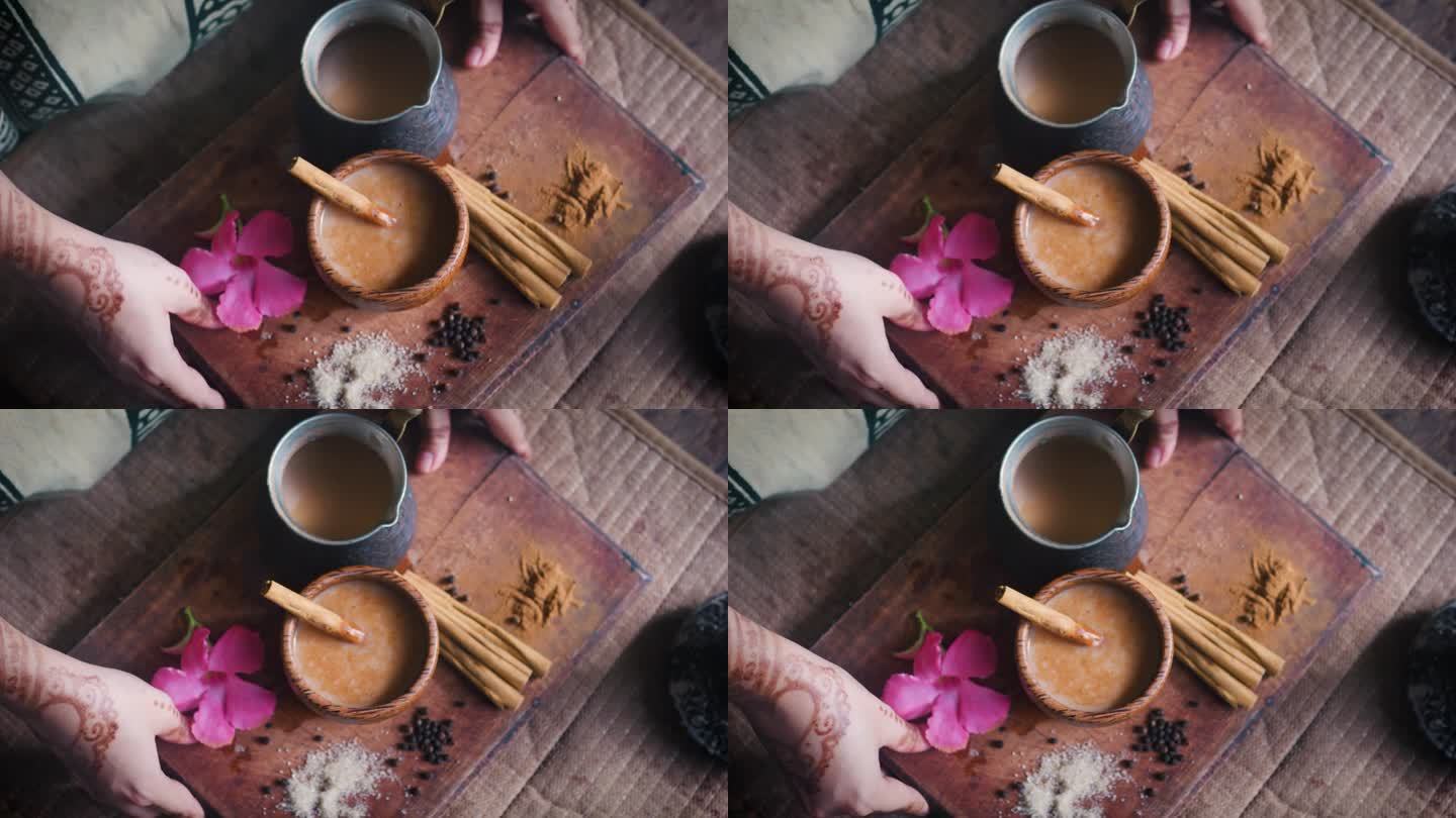 印度妇女用手把托盘木板和印度奶茶放在桌子上。