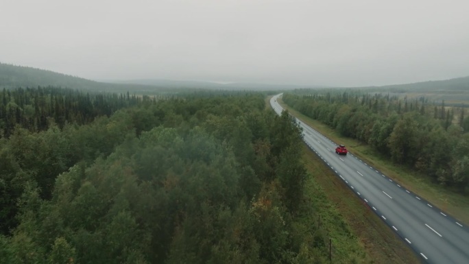 下雨天，无人机跟随红色SUV行驶在野外的道路上。