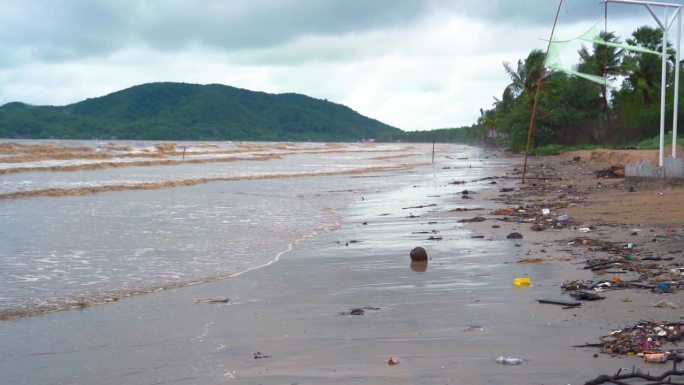 汹涌的海浪带着浑浊的海水和沙滩上的垃圾来到海滩上，同时暴雨。