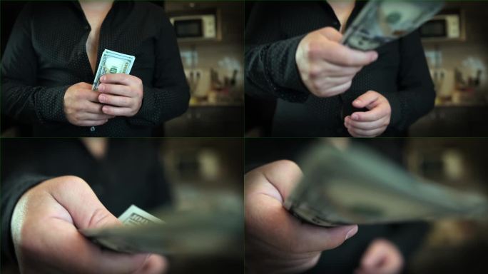 一名身穿黑色衬衫、未扣扣子的男子的特写镜头，他手里拿着一包100美元的钞票。