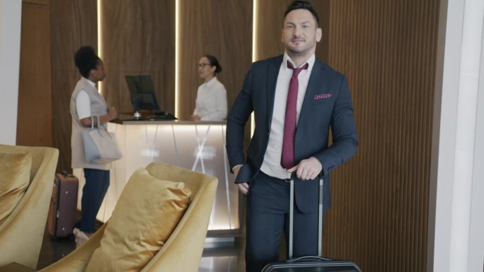 男企业家站在酒店大堂，提着行李箱，面带微笑