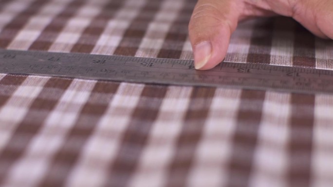 女裁缝正在用一把钢尺量格子布的尺寸，并在上面画上点，以便裁剪。