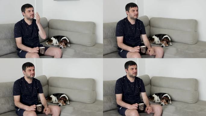 一个男人坐在沙发上，喝着咖啡，抽着烟，而他的杰克罗素狗，睡在他旁边
