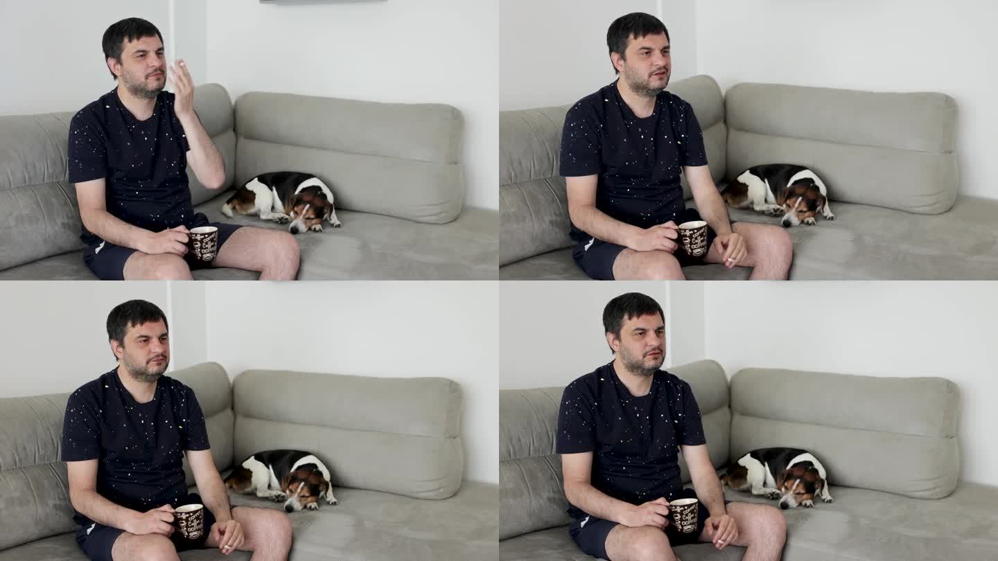 一个男人坐在沙发上，喝着咖啡，抽着烟，而他的杰克罗素狗，睡在他旁边