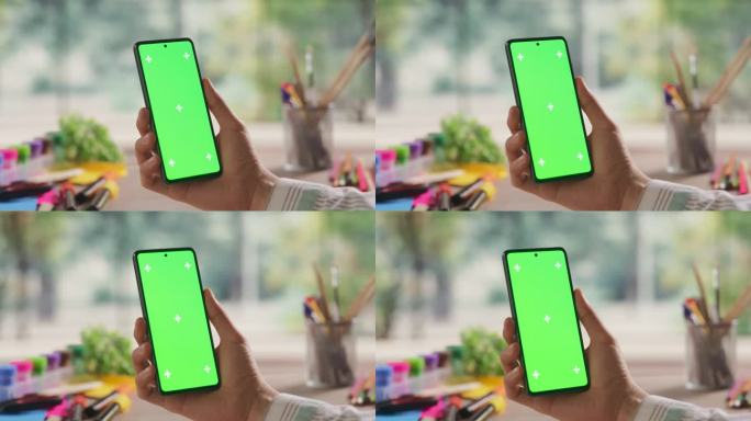 插画师拿着智能手机设备，看着屏幕与绿色Chromakey模拟显示。视频模板与数字营销，创意设计演示，
