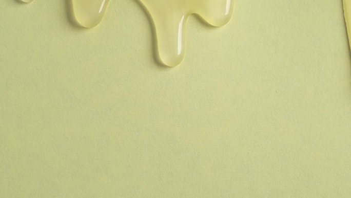黄色涂料化妆品的液体滴在黄色的表面上流动。淡黄色沐浴露滴在墙上的微距镜头