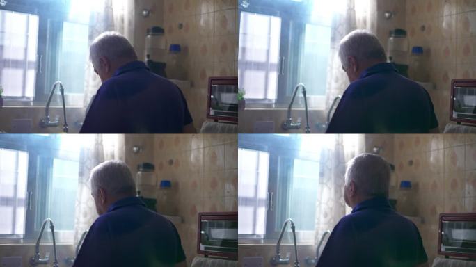 背后沉思的老人站在厨房窗边凝视着窗外，阳光照进来。老年人的沉思孤独情绪