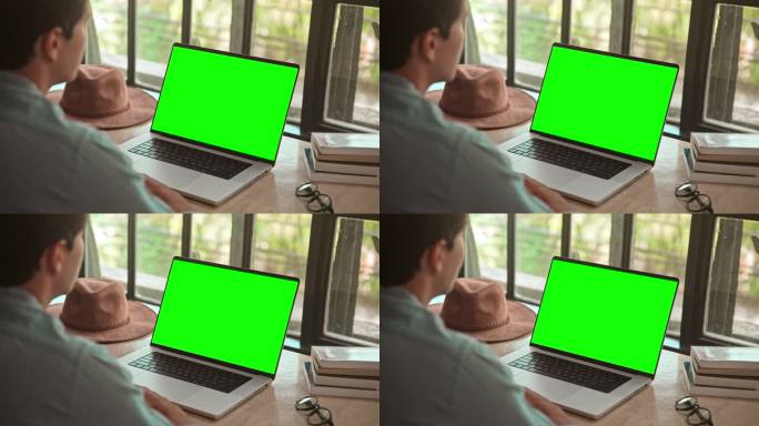 男人在笔记本电脑上工作，看着绿屏模拟色度键和视频通话。网络讨论中的远程办公和聊天特写。观看视频通话或