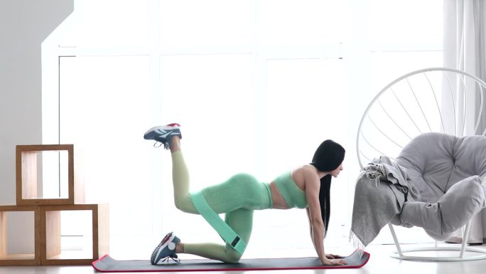 健身妇女在家用阻力带做提腿锻炼臀肌。运动女孩锻炼身体