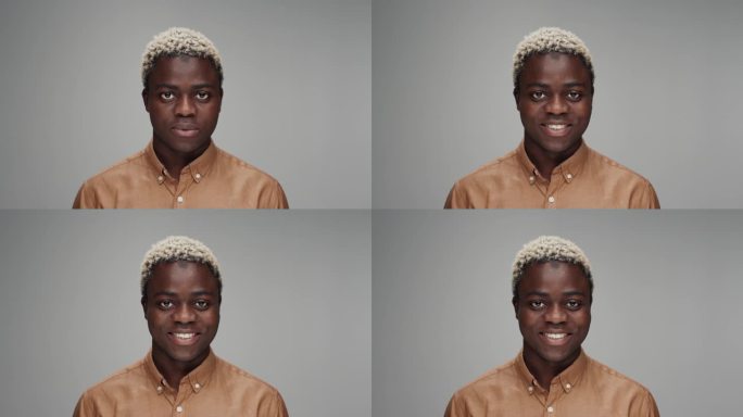 在彩色摄影工作室拍摄的年轻黑人男子看着相机微笑的肖像。成年非洲男孩孤独的灰色背景特写。20多岁的非裔