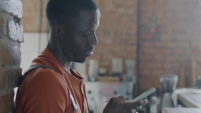 非裔美国人咖啡师使用智能手机触摸屏应用程序，在咖啡馆微笑