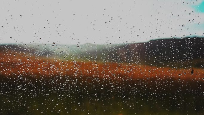 特写窗户上的雨滴，可以看到农村的麦田
