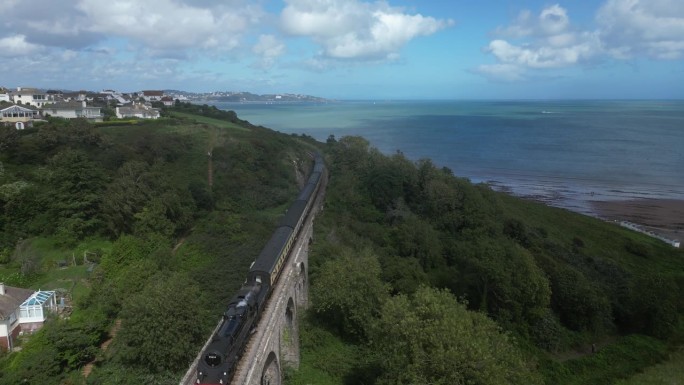 英国南德文郡，托贝，布罗德桑兹:无人机视野:一列蒸汽火车驶向王格伦，背景是托贝海