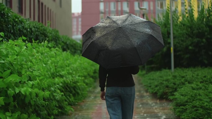 打着伞的女人在雨中行走。阴雨的夏日下着大雨，女孩撑着伞走在潮湿的道路上穿过城市。慢镜头