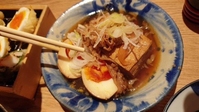 用手筷子吃小配菜的日本居酒屋料理豆腐炖牛肉和鸡蛋菜4k