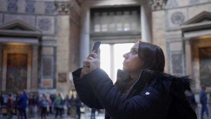 意大利罗马，身穿保暖夹克的年轻西班牙妇女用手机拍摄万神殿内部的照片