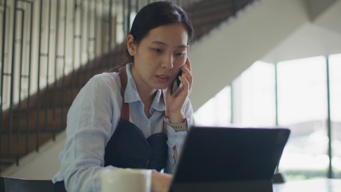 年轻女子在咖啡店工作时使用数码平板电脑和智能手机