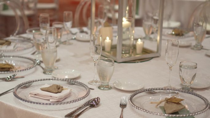 用鲜花装饰的婚礼圆桌。水晶盘子和玻璃杯，餐具，白色桌布和点燃的蜡烛在中心。
