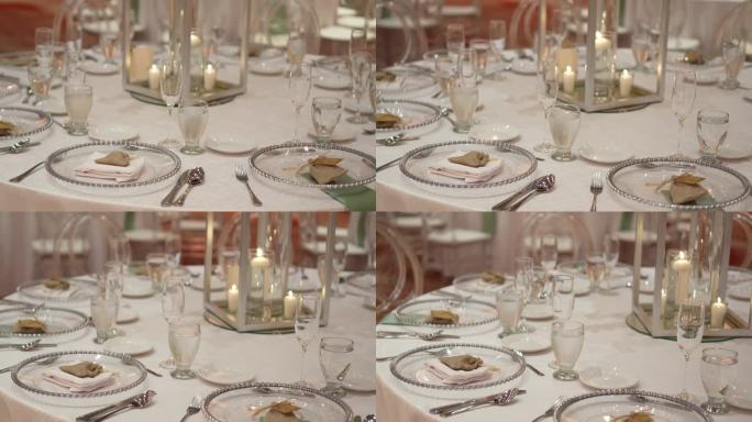 用鲜花装饰的婚礼圆桌。水晶盘子和玻璃杯，餐具，白色桌布和点燃的蜡烛在中心。
