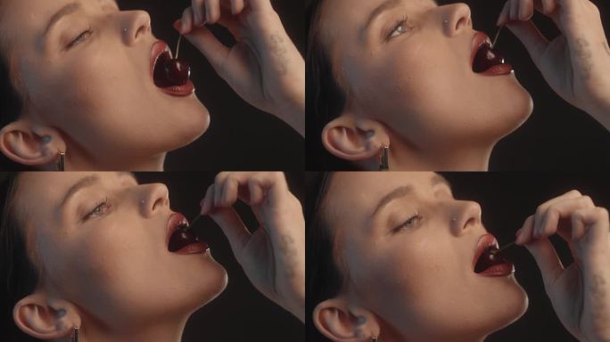 美丽性感的女人用红色的口红黑色的背景工作室拍摄咬一口樱桃
