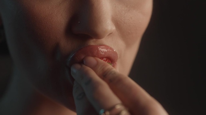 美丽的性感的女人用红色的口红工作室拍摄咬一口甜草莓