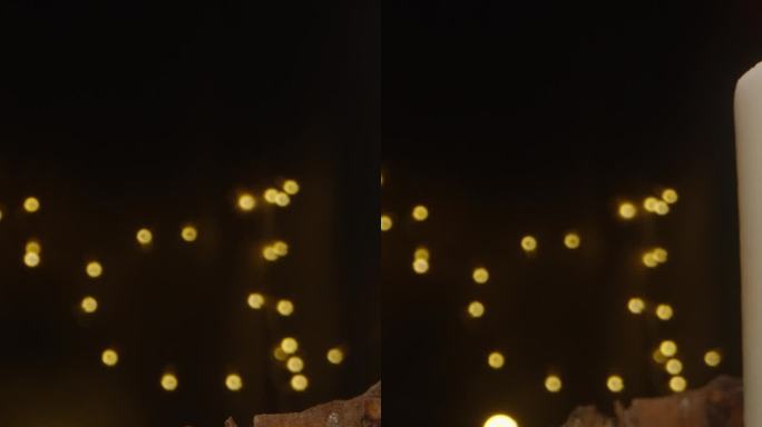 垂直视频。蜡烛在手工制作的新年装置中点燃，背景是黑暗中的花环。多莉滑块极端特写。