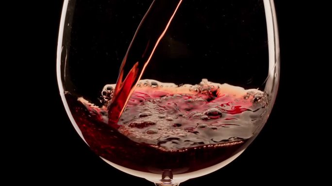 在黑色背景上，红酒正在倒进玻璃杯里。慢镜头，近景。伟大的葡萄酒背景为您的项目。