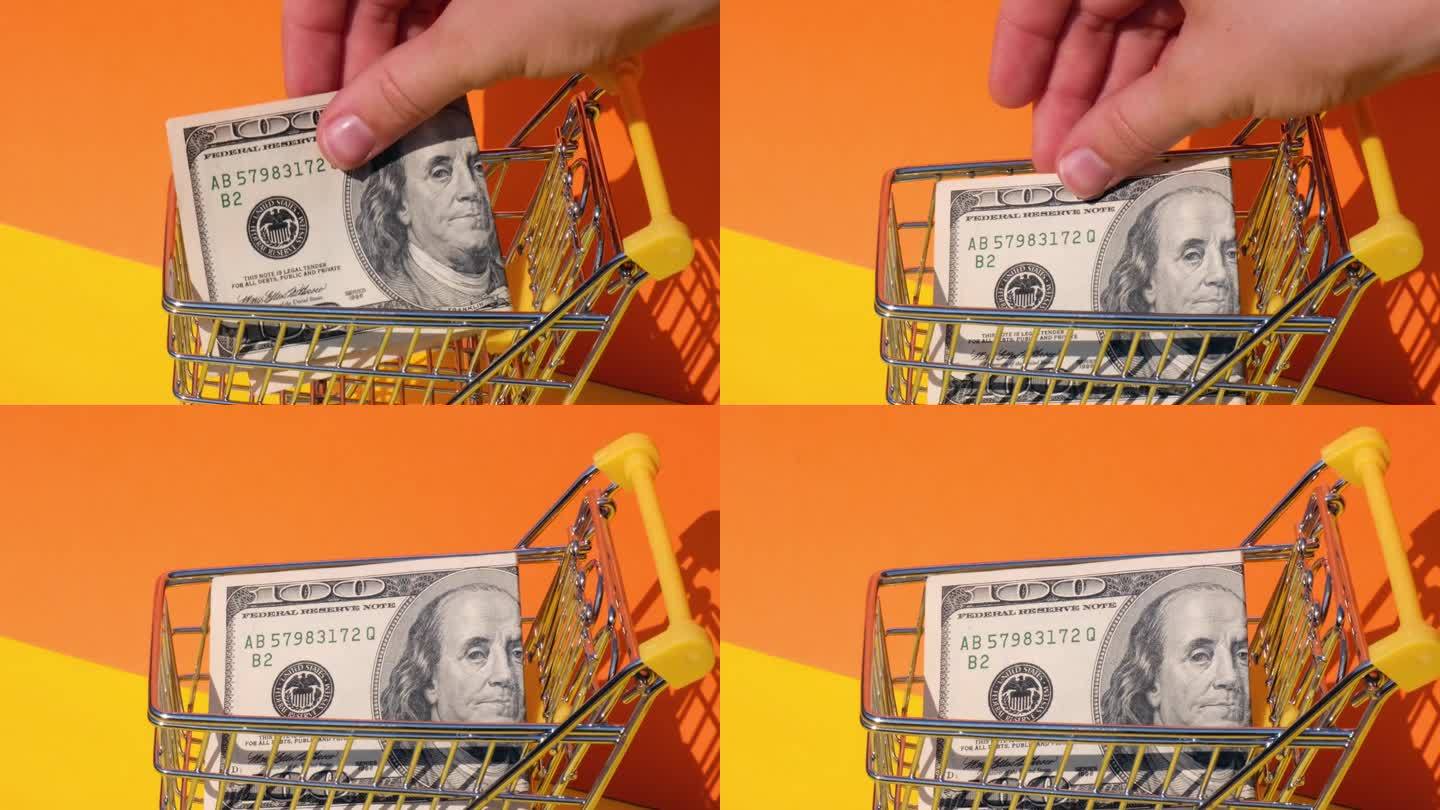 手加100美元钞票在玩具超市购物车黄色背景的钱。销售一篮子美元钞票。最低生活工资概念:贷款、投资养老