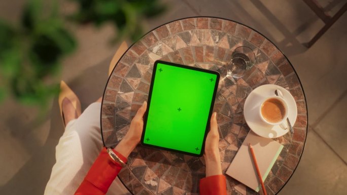 咖啡馆里，一位匿名女性使用带有绿屏Chromakey显示屏的数字平板电脑的俯视图。优雅的女人一边放松