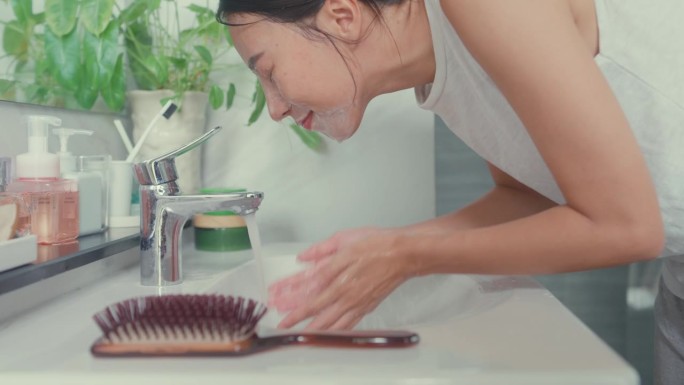 上午晚些时候，年轻的亚洲女人在家里的厕所里对着镜子用泡沫洗脸。日常的生活方式。