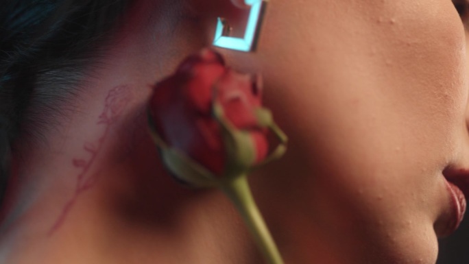 一个性感的女人涂着红色的口红和玫瑰纹身，在工作室里拿着一朵红玫瑰摆姿势，和镜头调情