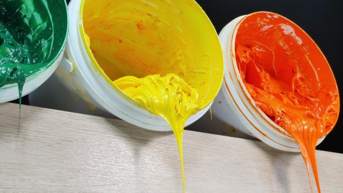 一个摄影车拍摄的绿色、黄色和橙色的油漆正从白色的桶里滴下来。