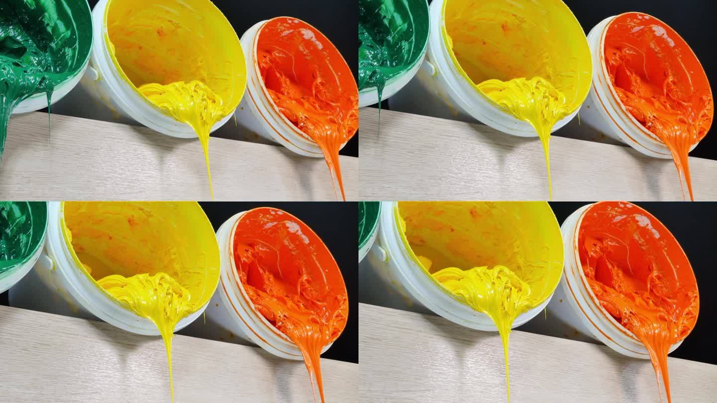 一个摄影车拍摄的绿色、黄色和橙色的油漆正从白色的桶里滴下来。