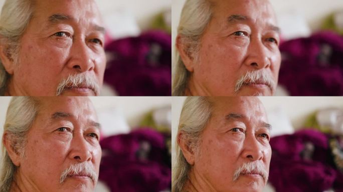 一位亚洲老人看电视，脸上带着严肃的表情。