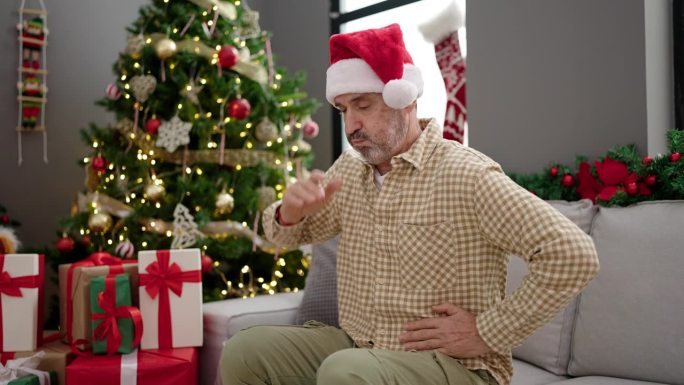 一名中年男子坐在家里圣诞树旁的沙发上恶心不已