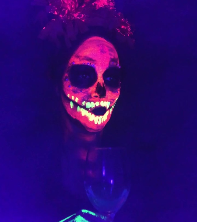 一名女子用霓虹灯画出骷髅形，参加墨西哥的亡灵节庆祝活动和派对，她的玻璃被黑光灯照亮