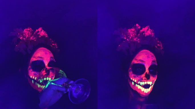 一名女子用霓虹灯画出骷髅形，参加墨西哥的亡灵节庆祝活动和派对，她的玻璃被黑光灯照亮