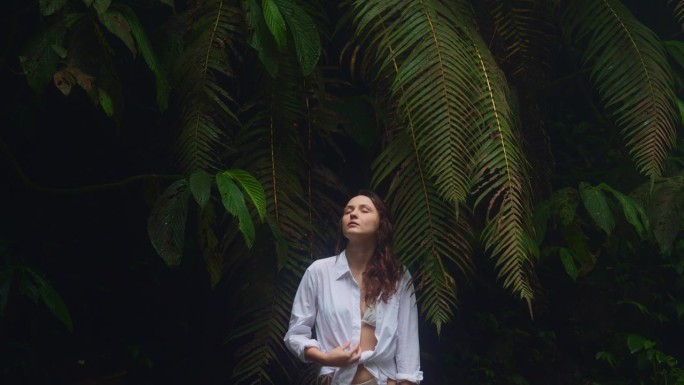 穿着白衬衫的禅宗女人站在茂密的热带树叶的背景上