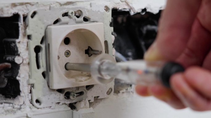 一个电工手持螺丝刀测试器对一个旧的坏插座进行相位检查