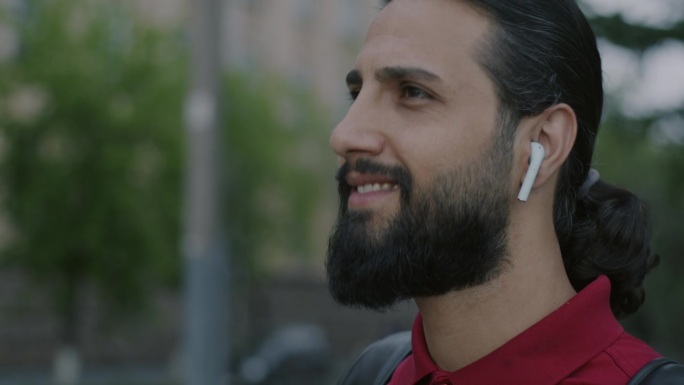 快乐的阿拉伯人的肖像，戴着无线耳机，听着音乐，在城市户外跳舞