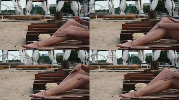 一位年轻女子正躺在躺椅上晒日光浴，并在腿上涂上防晒霜