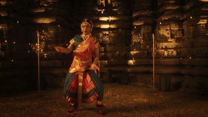 一位富有表现力的年轻印度舞者在一座古老的寺庙里表演民间舞蹈的慢动作肖像。穿着传统服装的妇女穿着五颜六