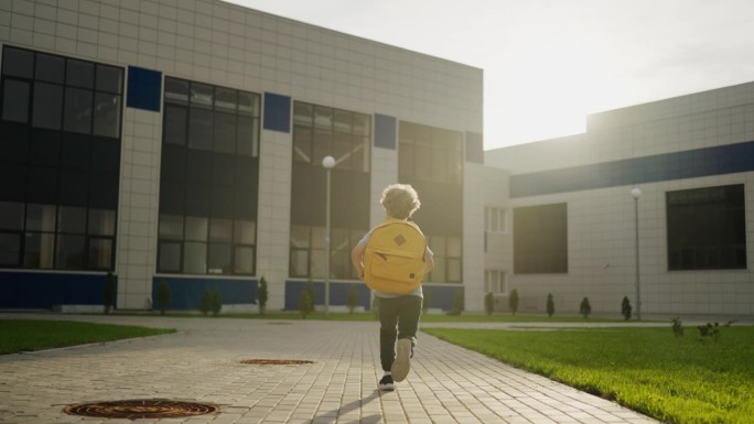 孩子男孩跑到学校的现代建筑，后视图，慢动作，快乐的情绪，去上学