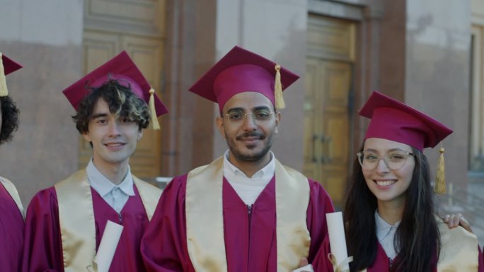 身着长袍、头戴毕业帽的多民族人群站在校园里，手里拿着毕业证书，面带微笑