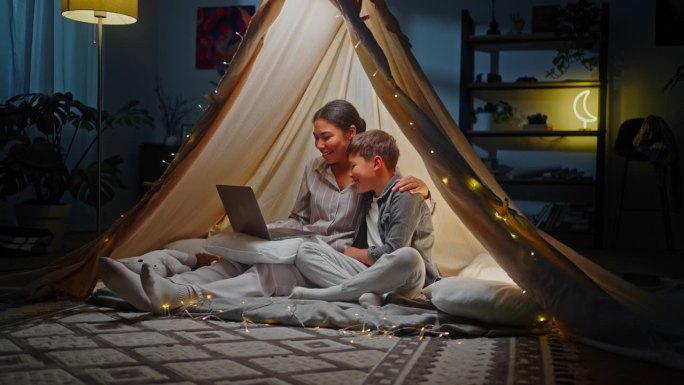 妈妈和儿子坐在家里的游戏帐篷里，用笔记本电脑进行视频通话。人。技术。家庭