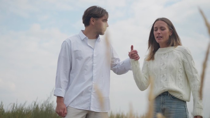 自信的男人和女人分手的照片，悲伤的女人站在秋天田野的右边，双手交叉，望向远方。年轻的白人夫妇分手。