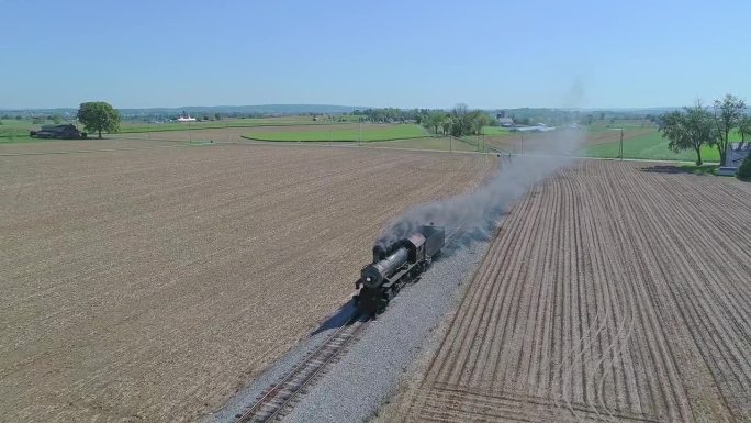 无人机拍摄的一列热气腾腾的火车行驶在乡村之间的铁路上