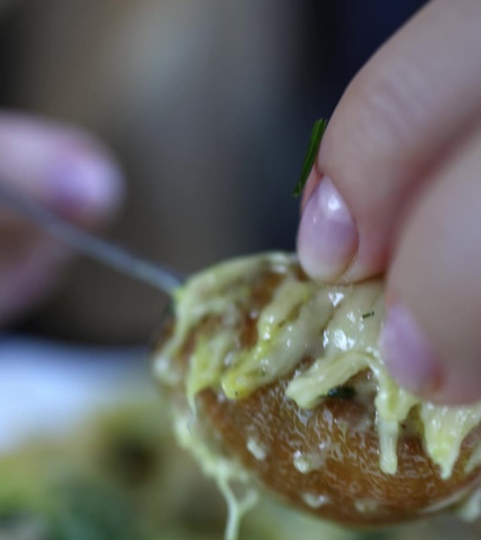 女性的手用叉子把蜗牛从海螺壳里拽出来。宏。垂直视频。这个女孩吃蜗牛配奶酪